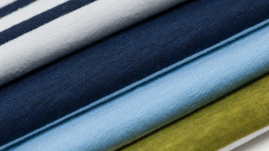 Detalhe de tecidos em diferentes cores e texturas, ideais para confecção de camisetas e uniformes personalizados.