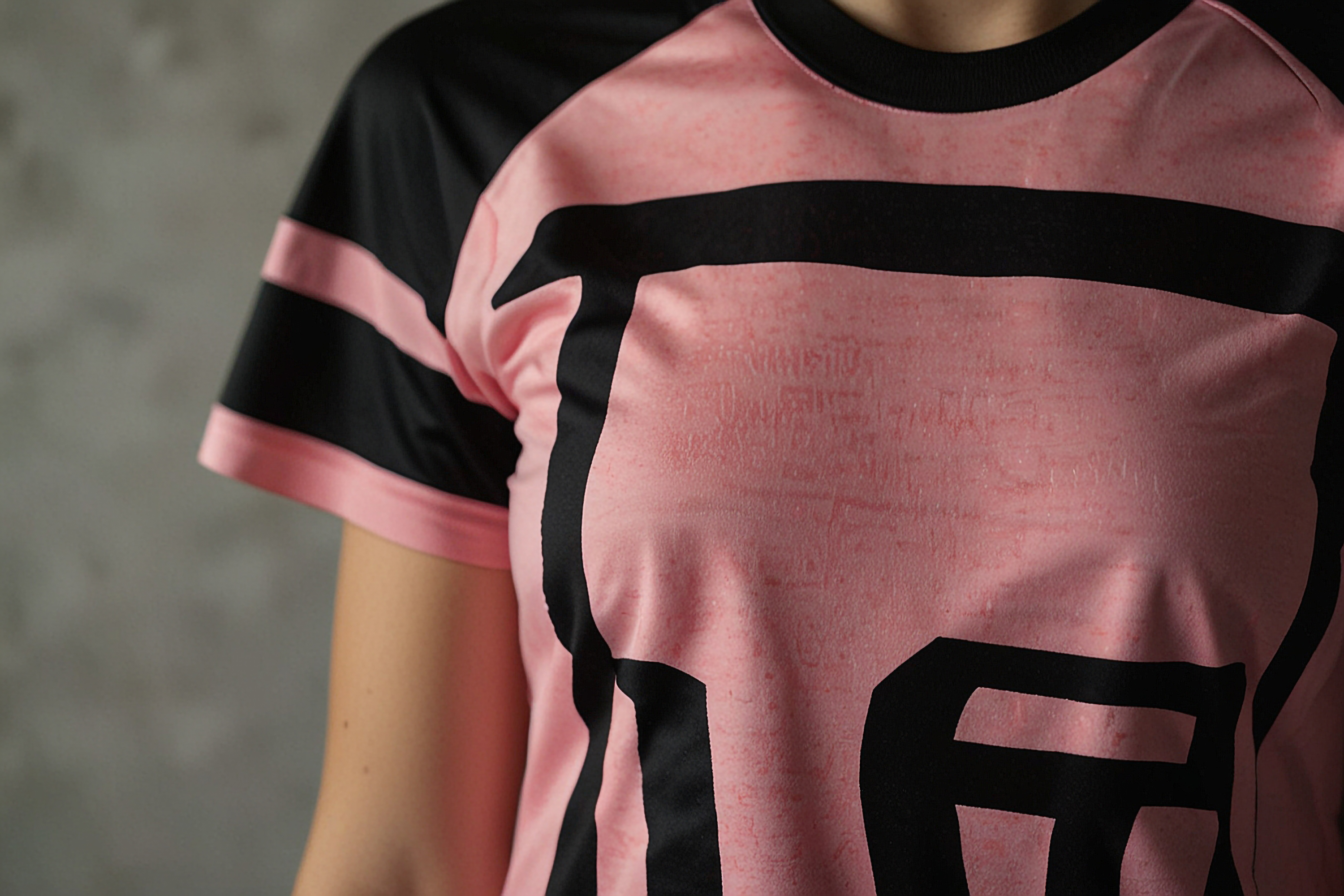Camiseta esportiva rosa com detalhes em preto, vestida por uma pessoa, destacando o design moderno e o tecido esportivo.