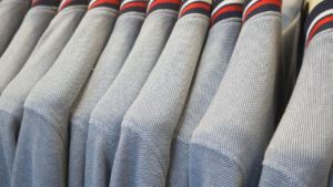 Uniformes escolares azuis pendurados em cabides, organizados lado a lado, com detalhe de gola listrada.